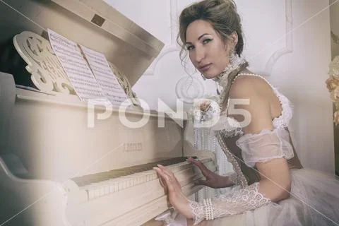 A young woman in an 18th century dress and lace in the boudoir sits at ...