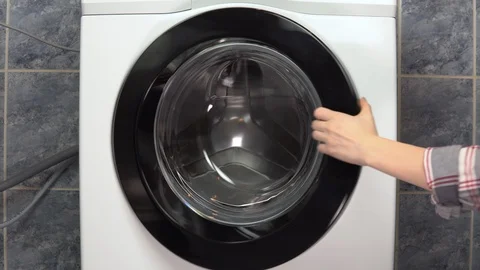 A young woman is actively loading clothes with a washing machine. The woman Stock Footage 125913445
