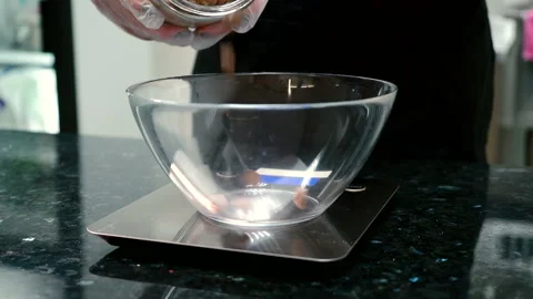 Young woman is adding chocolate biscuits into bowl on scales in kitchen. Stock Footage 88570603