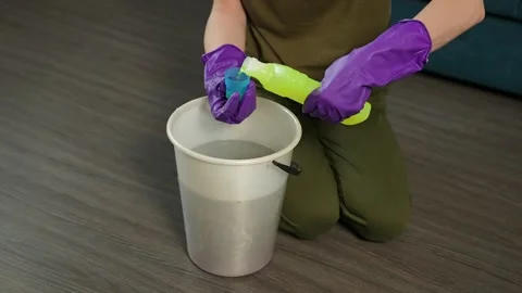 A young woman is adding a cleaning solution to a bucket of water. A concentrated Stockbeeldmateriaal 306124197