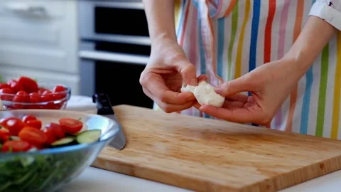 Young woman adding mozarella to vegetable salad in the kitchen Stock Footage 88126626