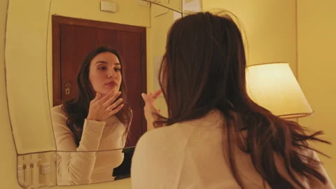 Young woman adjusting makeup while standing in front of mirror at home Stock Footage 229508960