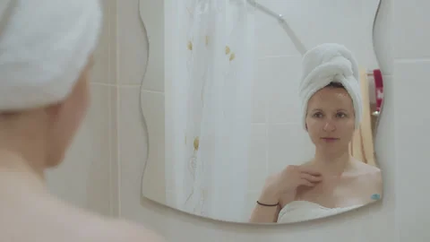 Young woman applying creme on face near mirror in bathroom 2 Stock Footage 276854853