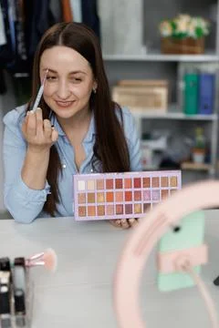 Young woman applying makeup on face with brush while recording vlog for social Stock Photos