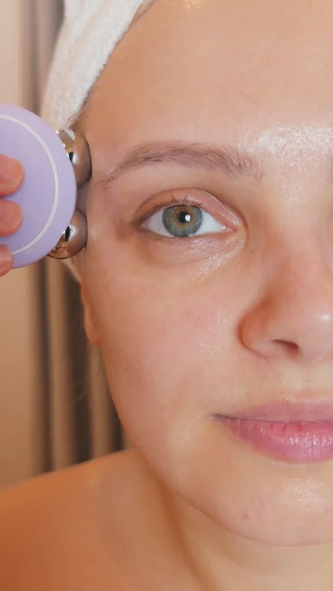Young woman applying microcurrent device to her face, focusing on anti aging Stock Footage 340522293