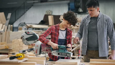 Young woman apprentice learning to use electric polisher in wood workshop Stock Footage 113745064