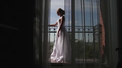 A young woman approaches the window, opens to a balcony, enjoying. morning bride Stock Footage 81715427