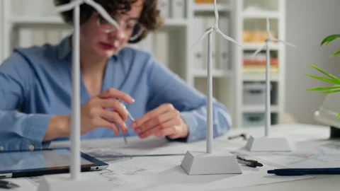 Young woman assembling miniature wind turbines in a modern workspace during Stock Footage 323717383