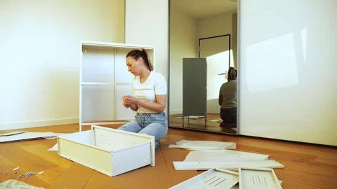Young woman assembling white flat pack furniture at home Stock Footage 319405832
