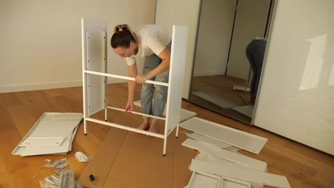 Young woman assembling white flat pack furniture at home Stock Footage 319406094