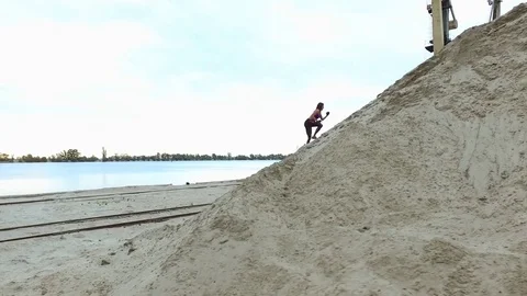 Young woman athlete climbs a sandy mountain. On the background can be seen the Stock Footage