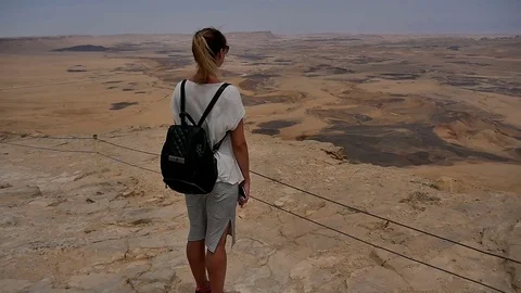 Young woman with backpack standing on cliff's edge and enjoying the desert view Stock Footage 76927034