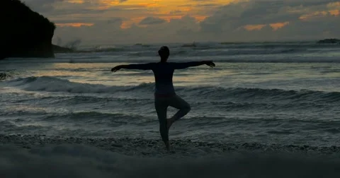Young woman balances in yoga position at sunset / sunrise on beach Stock Footage 59136848