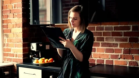 Young woman in bathrobe doing notes while standing in the kitchen Stock Footage 91155124