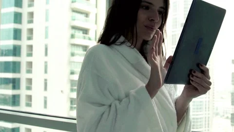 Young woman in bathrobe using tablet computer by window at home Stock Footage 87670654