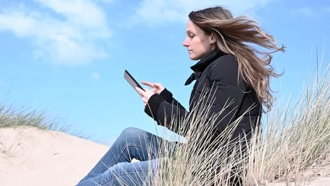 Young woman beach dune using a tablet on a winter windy day Video stock 103755013