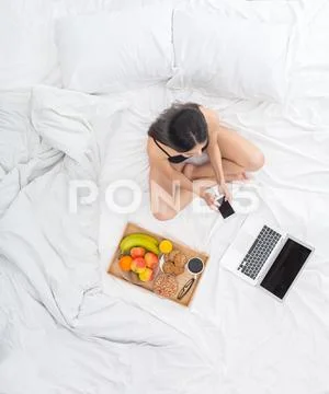 Young woman on bed top view breakfast concept playing smartphone Stock Photos