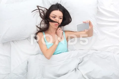 Young woman on bed top view morning concept taking selfie photos posing Stock Photos