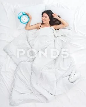 Young woman on bed top view morning concept looking at alarm clock Stock Photos