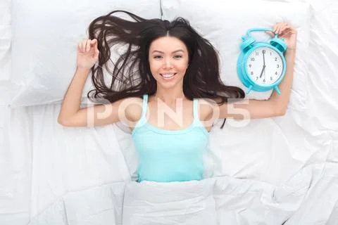 Young woman on bed top view morning concept close-up holding alarm clock Stock Photos