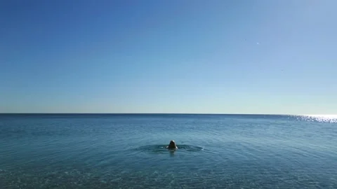 Young woman begins to swim away into the sea, the camera follows her from behind Stock Footage 228301008