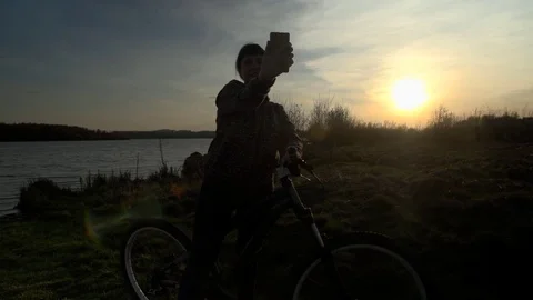 Young woman bicyclist uses phone at sunset. Stock Footage
