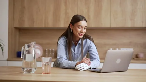 Young woman with bionic hand is talking in front of laptop and standing at table Stock Footage 200105471