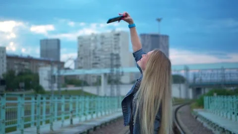 A young woman, blonde, on the railway tracks, takes a selfie en a smartphone. Stock Footage