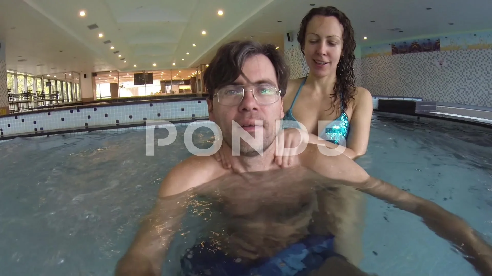 Young woman in blue bikini massages man man makes selfie in pool