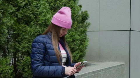A young woman in a blue jacket using smartphone by parapet and thujas. Stock Footage 273015362