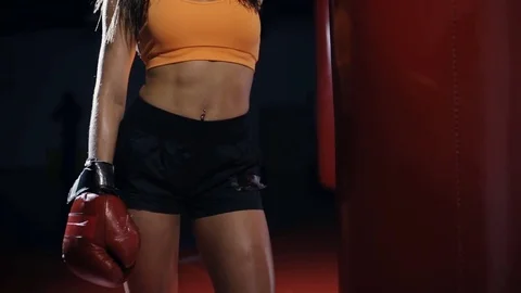 Young woman boxer standing at punching bag in a dark hall Stock Footage