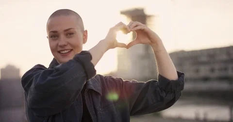 Young woman with buzz cut making a hearth with her hands into the sunlight in Stock Footage 83248089