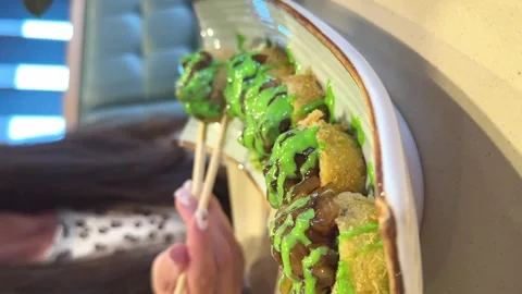 Young woman in a cafe eats backed rolls with sauce with wooden sticks. Vertical Stock Footage 265016331