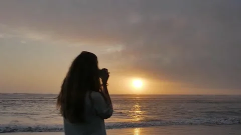 Young woman with camera on beach side during sunset Stock Footage 143423655