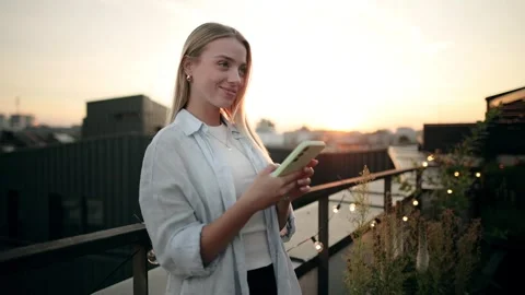 A young woman is casually using her smartphone while enjoying a beautiful sunset Stock Footage 281632899