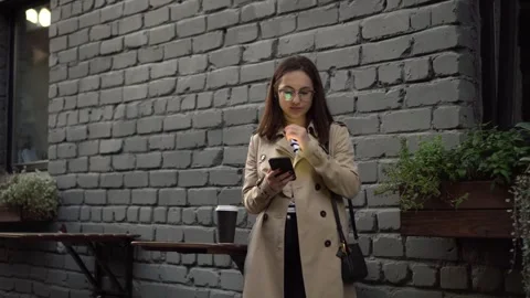 A young woman is chatting on a smartphone while standing against a wall on a Stock-Footage 252401577