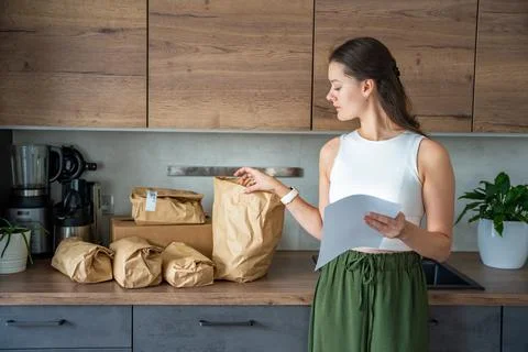 Young woman checking a list while looking at unpacked meal kit ingredients Stock Photos
