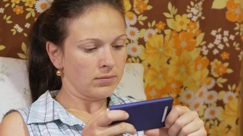 A young woman is checking messages on a mobile phone at home on the couch. Stock Footage 76990945