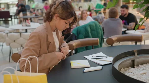 Young woman checking phone for reference notes at cafe table, balancing shopping Stock Footage 322906485