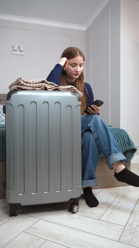 Young woman checking smartphone next to packed suitcase on bed Stock Footage 309775305