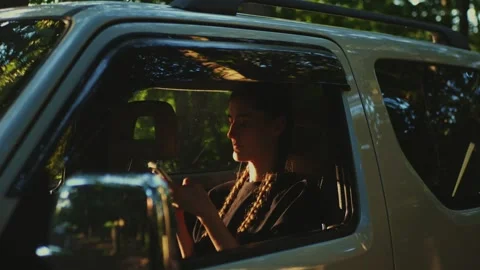 Young woman checking a smartphone while sitting inside a parked... 库存影片 341613086
