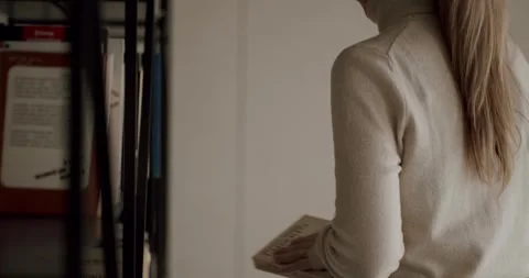 Young woman choosing and pulling a book from a bookshelf Stock Footage 345543289