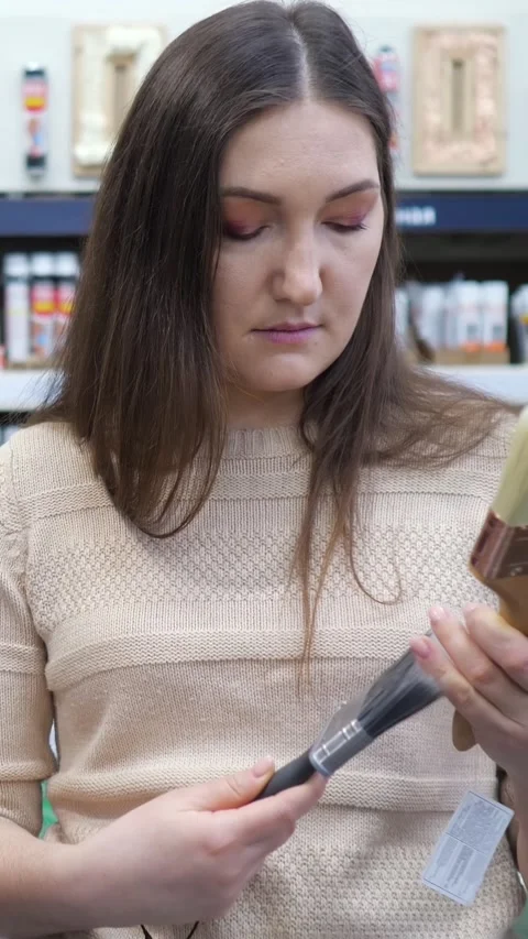 Young woman choosing between two different paint brushes in a hardware store for Stock Footage 346096566