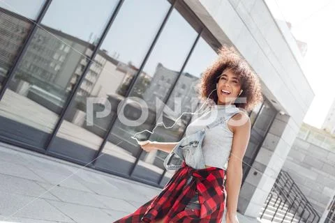 Young woman in the city street near window with smartphone wearing earphones Stock Photos