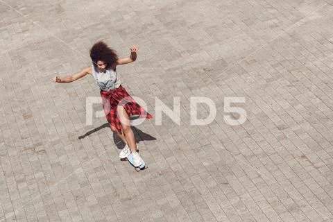 Young woman in the city street riding penny board hands up cheerful top view Stock Photos