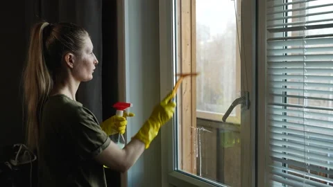 A young woman is cleaning a window using a cleaning solution and a squeegee. A Видео 306157926