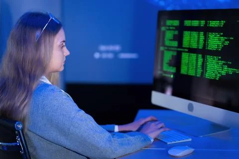 Young woman coding on a computer in a modern tech environment during evenin.. Stock Photos