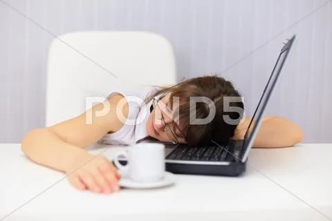 Young woman comically sleeps on laptop at office Stock Photos
