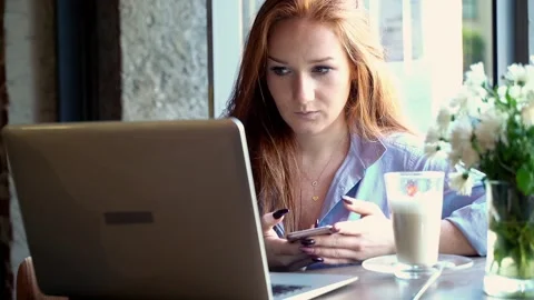 Young woman comparing data on smartphone and laptop in cafe Stock Footage 88583109