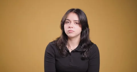 Young woman with concerned expression sitting in front of a yellow background Stock Footage 346664232